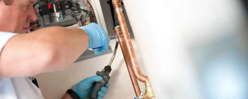 Water heater repair technician testing copper pipe connections and controls in Mesa, AZ